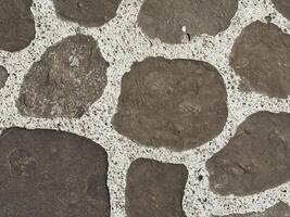 Close-up of a vintage-style stone pavement with irregular dark rocks embedded in bright cement, evoking retro charm and rustic courtyard ambiance Textured Stone Wall Close-Up photo