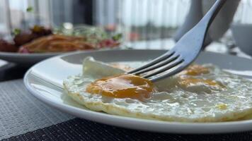 take a runny yolk from a white plate with a fork For breakfast Fried eggs on a plate video