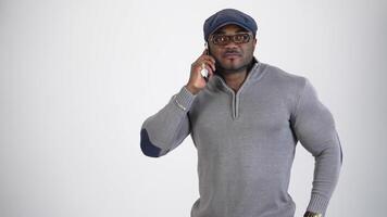 Portrait of black skinned athlete with a mobile phone. Athletic afro american guy wearing stylish glasses and cap talking the phone with gestures on white background. video