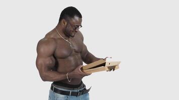 Black skinned sportsman with pizza. Muscled african man in glasses without shirt holding a box and taking out a piece of pizza in studio. video
