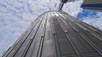 Large metal grain elevator outdoors. Modern silver granary on sky background. Huge aluminum container for storing crop. View from below. video