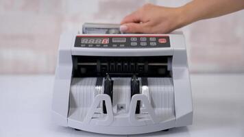 Equipment for counting money. Wad of hundred dollars are counted in a calculating machine. Automatic equipment for banking financial transactions. Female's hand puts money into electronic machine. video