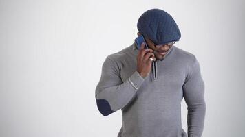 Smiling black skinned man doing a phone call. Happy young african man wearing glasses and cap talking the phone isolated on white in studio. video