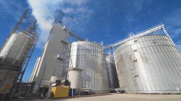 Panoramic view of agricultural plant. Large round grain elevators for storing grains. Thick fumes releasing into the air during grain processing on a factory. video