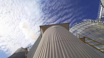 Metal grain elevator on sky background. Large granary for storing cereals. Thick smoke releasing into the air from industrial plant. Pollution. View from below. video