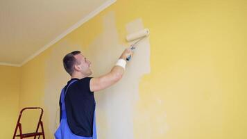 Room renovations at house. Paint being applied on a wall by a professional worker. Painter man painting the wall at home with paint roller and creamy color paint. Side view. video