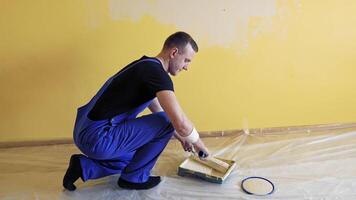 Painter rolling paint roller in color on a tray. Handyman working with a paint roller and having a pain in back. Renovation at home. video