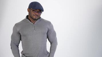 Smiling afro american athlete in studio. Portrait of a sportive guy with black skin in gray sweater and blue cap looking on camera. Copy space. video