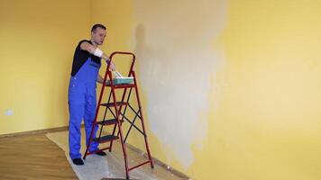 Young man in overalls renovating room in the house. Painter worker using a paint roller doing makeover of a room. Room decoration with new color. video