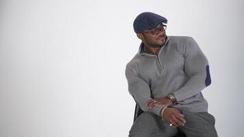 Handsome black man with trained body in studio. Portrait of a black skinned guy sitting on chair and looking aside. Afro american businessman isolated on white. Copy space. video