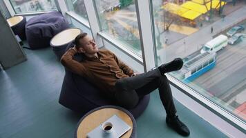 Businessman relaxing in office. Young man sitting in comfortable armchair with closed eyes and dreaming at daytime next to the window with city view. Top view. video