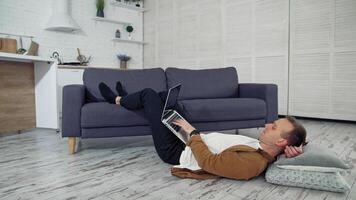 Freelancer works on laptop on floor. Tired young businessman lying on a floor and puts aside the laptop after the long job at home. Distant job during quarantine. video