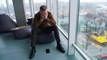 Businessman sitting in office by the large window. Thoughtful man with his hands on eyes becomes happy after finding the solution to the problem. video