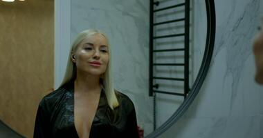 girl in a stylish bathroom stands in front of a mirror wearing headphones. She looks thoughtful and composed preparing herself as the evening unfolds. The ambiance is serene and contemporary video