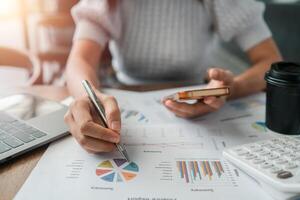 Professional woman reviewing financial charts and graphs with a smartphone and laptop, emphasizing business analysis. photo