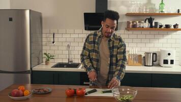 African-American man dancing joyfully in the kitchen while preparing a salad. Wearing headphones, he listens to music, sings along, and points playfully toward the camera. video
