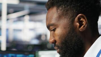 Server farm computer scientist interprets data analytics graphs. African american man in data center using artificial intelligence program showing predictive system metrics, camera B video
