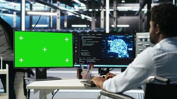 Data center engineer with paraplegia using AI deep learning algorithms on green screen PC to analyze datasets. Server room worker in wheelchair at chroma key PC using AI neural networks, camera B video
