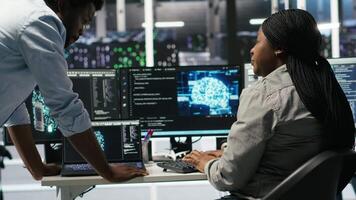 Data center engineering team uses artificial intelligence deep learning models to configure gear. Teamworking colleagues work on AI programming language in server farm, optimizing system, camera B video