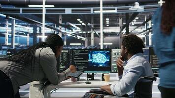 Admin in wheelchair and data center coworker working together using AI node tree software to minimize downtime. Server hub IT expert in disability and colleague using visual programming app, camera A video