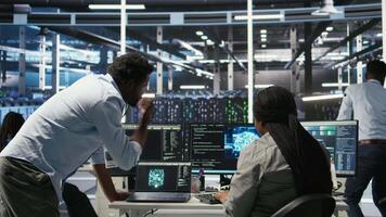 Data center engineering team uses artificial intelligence deep learning models to configure gear. Teamworking colleagues work on AI programming language in server farm, optimizing system, camera A video