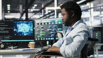 Engineer using wheelchair in data center using AI node tree software to minimize system downtime. Server hub worker in disability using visual programming to monitor performance, camera B video