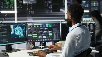 Data center admin using artificial intelligence neural network models to configure hardware. Man works on AI programming language in server room, optimizing system functionality, camera B video