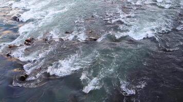 The river water flows swiftly, crashing against rocks, creating splashes and ripples in a dynamic and powerful natural scene video
