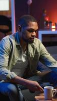 Vertical Male freelancer multitasking at home solving tasks with music on headset, listening to his favorite songs and paying attention to his remote work. African american guy enjoys schedule. Camera B. video