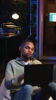 Vertical Black man joining online lesson to work on new skills from home space, attend web conference call and watching lecture from loft. Person participates at a virtual training class. Camera A. video