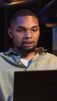 Vertical Black male freelancer taking online course to learn new skills from home, attend online call and watching lecture from loft. Young man participates at a virtual training class. Camera B. video