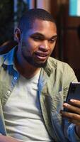 Vertical African american teleworker calling coworker on conference to take notes, writing new ideas and exchanging information on web meeting in the living room. Textbook data. Camera B. video