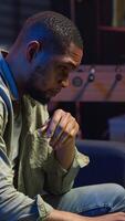 Vertical African american guy being overworked with headache at modern loft, working remotely under stress and pressure from his boss. Young person frustrated and worried, struggling with tasks. Camera B. video