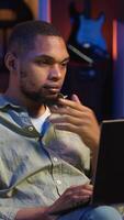 Vertical African american man working remotely from his modern loft on laptop, focusing on tasks completion while he lays on a bean bag. Blending productivity and relaxation, telework. Camera B. video