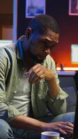 Vertical African american guy being overworked with headache at modern loft, working remotely under stress and pressure from his boss. Young person frustrated and worried, struggling with tasks. Camera A. video