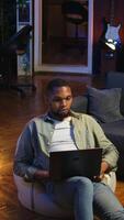 Vertical Young black person waving on remote call on laptop sitting at home, joining an online conference webinar to discuss about solving tasks. Teleconference in the living room. Camera A. video