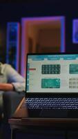 Vertical Black remote worker navigating on tablet next to screen running analytics, sitting at home working on his daily tasks with multiple devices. Leisure and job productivity in loft. Camera A. video