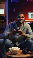 Vertical POV young black adult enjoying free time playing shooter games on smart tv, plugging console in the living room and spending game session at night. Man engaging in fun activity. Camera A. video
