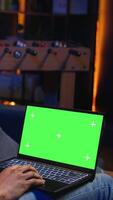 Vertical African american young guy using device with green screen from his sofa, enjoys the comfort of his modern cozy home. Casual relaxed person working in the living room, multitasking. Camera A. video