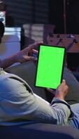 Vertical Black remote worker looking at green screen on his device at home, relaxing in the living room and solving freelancing tasks. Guy being casual in trendy apartment, teleworking. Camera A. video