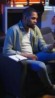 Vertical African american teleworker calling coworker on conference to take notes, writing new ideas and exchanging information on web meeting in the living room. Textbook data. Camera A. video