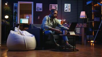 Male freelancer multitasking at home solving tasks with music on headset, listening to his favorite songs and paying attention to his remote work. African american guy enjoys schedule. Camera A. video