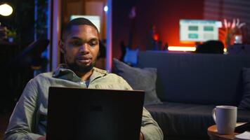 Kerl Überprüfung finanziell Balance und Arbeiten auf Buchhaltung Analyse, gewährleisten Unternehmen Einnahmen Wachstum beim heim. afrikanisch amerikanisch Arbeiter genießt Fernbedienung Job mit Wirtschaft Statistiken. Kamera a. video