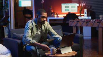 Male freelancer multitasking at home solving tasks with music on headset, listening to his favorite songs and paying attention to his remote work. African american guy enjoys schedule. Camera B. video