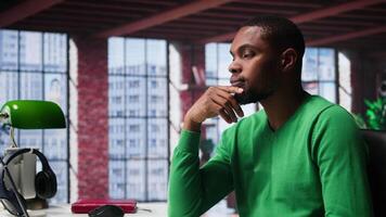 African american guy thinking about new ideas to increase clients numbers, multitasking to find a solution for financial growth. Young remote worker uses his creativity. Camera B. video
