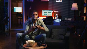 Male gamer eating popcorn while he plays online shooting tournament, having fun with games in his free time at home. Relaxed guy enjoying game night with snacks and competition. Camera A. video