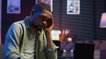 African american person receiving some bad news while doing remote work tasks, feeling overworked and under pressure to complete all his assignments. Young adult deals with burnout. Camera B. video