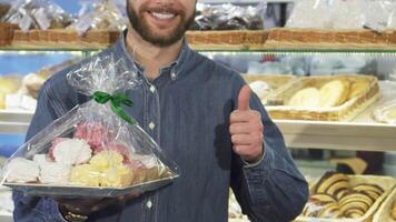 Cheerful bearded man giving thumbs up with a tray of colorful desserts video