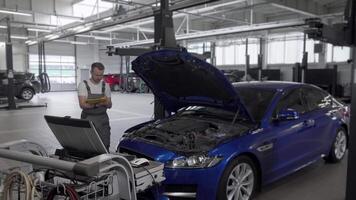 Mature male mechanic diligently taking notes and using computer while repairing a car video