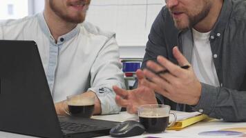 Engaged male colleagues enjoying coffee while discussing work video